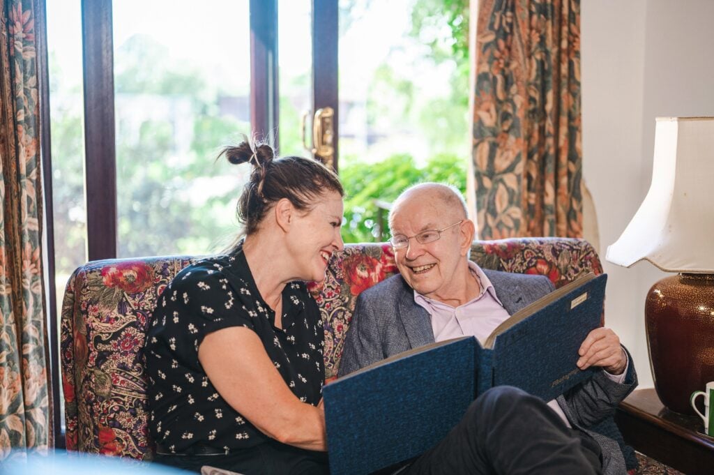 An iCare4U carer looking through a photo album with an older man in his living room