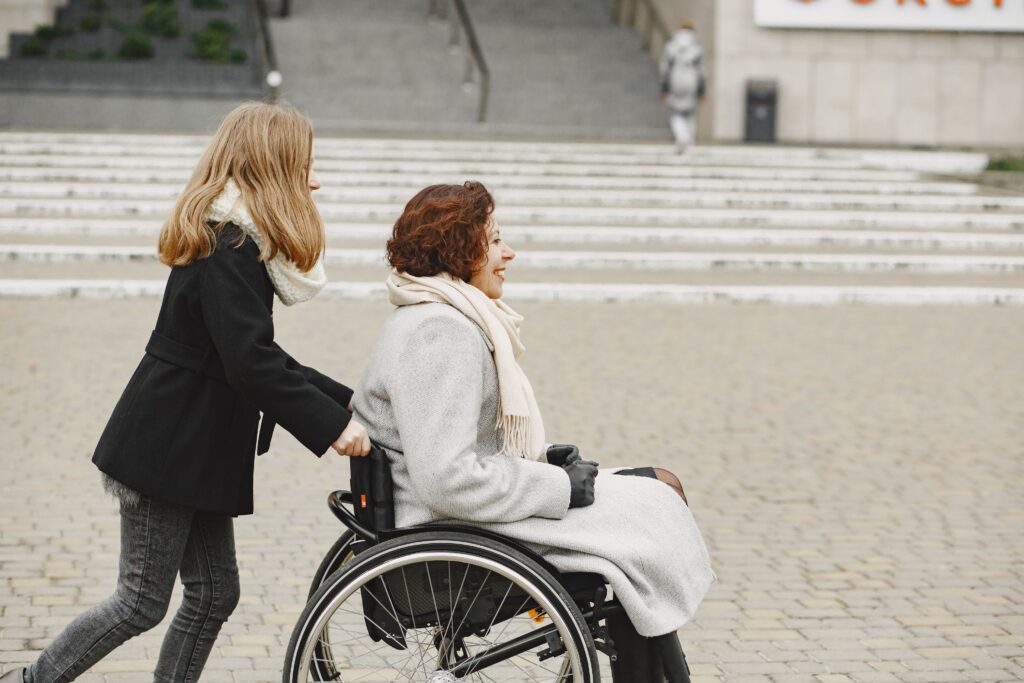 A support worker assisting a woman in a wheelchair along a footpath outdoors