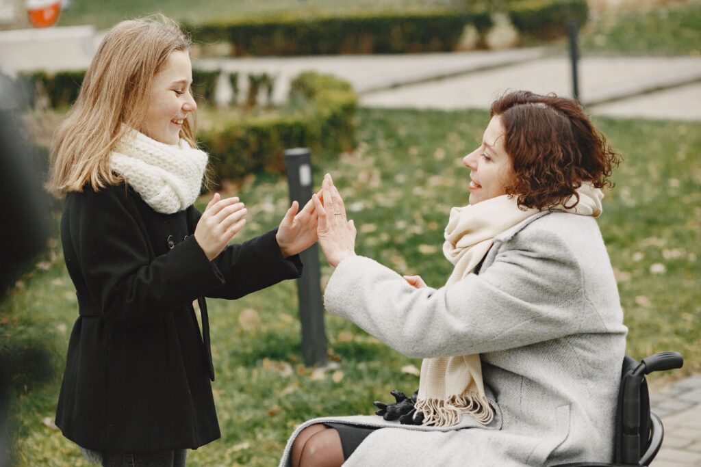 Two women outdoors, one using a wheelchair, holding hands and smiling in Dandenong