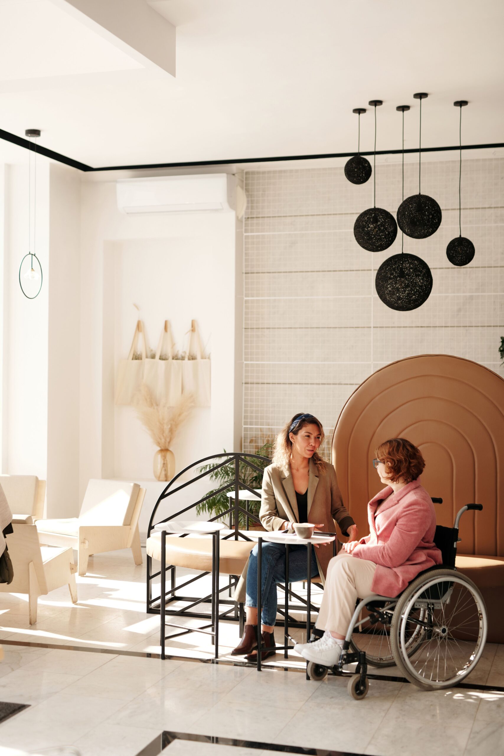 A support coordinator talking with an NDIS participant who uses a wheelchair, over coffee
