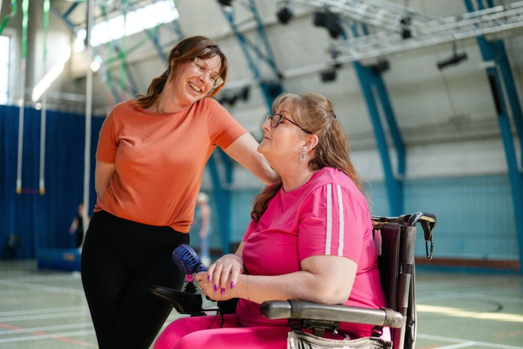 A support worker and a woman who uses a wheelchair smiling together